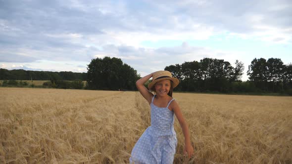 Cute Happy Child in Straw Hat Jogging Over the Meadow of Barley, Beautiful Girl with Long Blonde