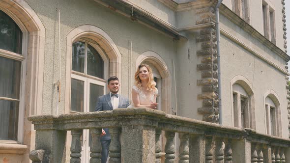 The Groom Approaches the Bride Standing By the Stone Balcony and Hugs Her From Behind. Happy