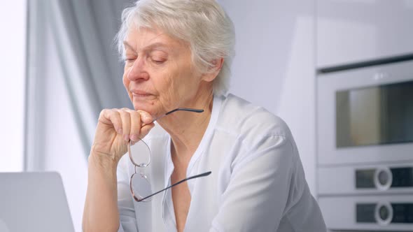 Thoughtful senior lady secretary with short hair holds glasses in hand