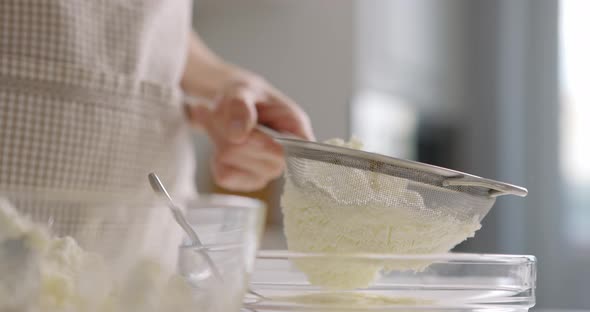 Woman in Gray Apron Rubs Cottage Cheese with Sieve at Home Kitchen