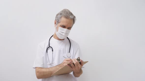 Elderly Doctor Man Makes Notes Wearing Stethoscope Isolated on White