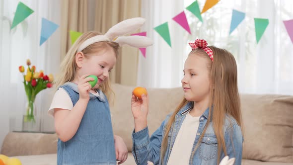 Little Girls with Rabbit Ears Play with Easter Eggs in Game of Who Will Break
