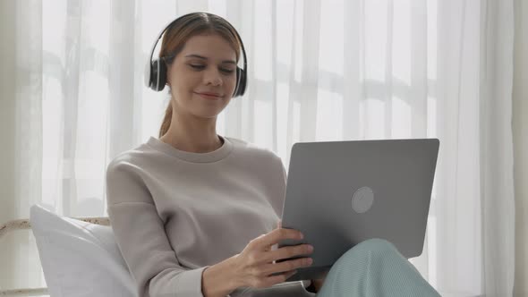 Happy young woman wearing headphones listening music while using laptop computer and singing.