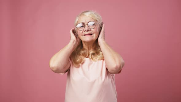 Attractive Senior Woman in Glasses Preening Looking at Camera As Mirror Pink Studio Background