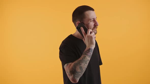 Young Man with Tattooed Arms Has a Conversation Through Smartphone Looking Away Studio Shot Copy