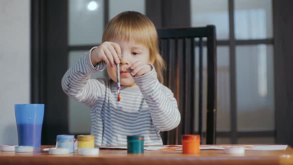 The Kid is Engaged in Drawing with a Brush Using Gouache Paints