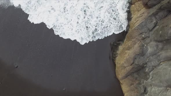 Aerial view of splashes and swashes of waves on cliff rocks at volcanic beach seashore. White foam b