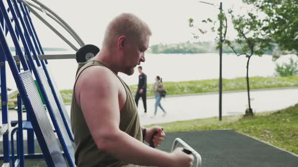 Strong Man Performs Exercises for Muscles on Exercise Machines in Outdoor Gym