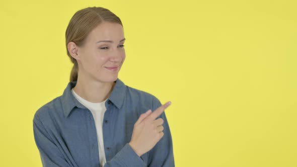 Young Woman Pointing Towards Product on Yellow Background