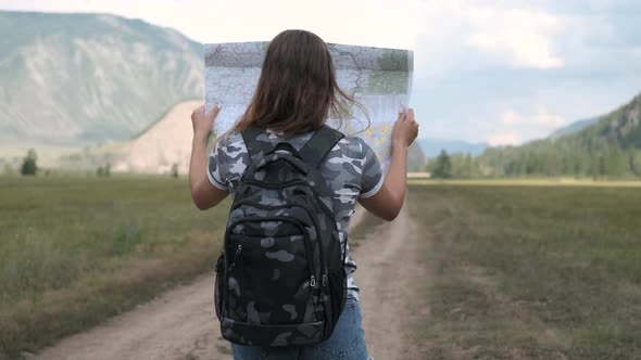 Attractive Woman Tourist Goes on the Road with a Map in His Hands on a Background of Mountains