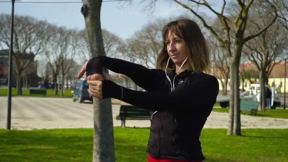 Beautiful Concentrated Sportswoman Stretching Hands in Park