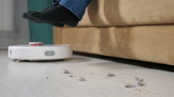 Man Lift Feet Up When a Smart Vacuum Cleaner Passes to Clean the Floor