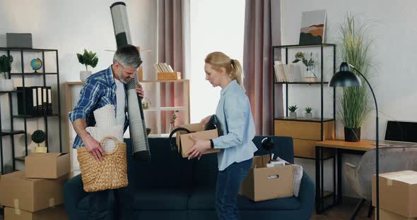 Adult Couple Holding Boxes and Basket with Home Decor and Starting to Furnish their New Apartment