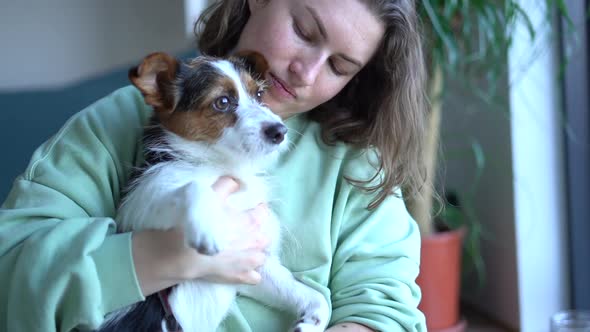 Smiling Caucasian Woman Kissing and Cuddling Her Pet Dog Sitting on Floor at Home