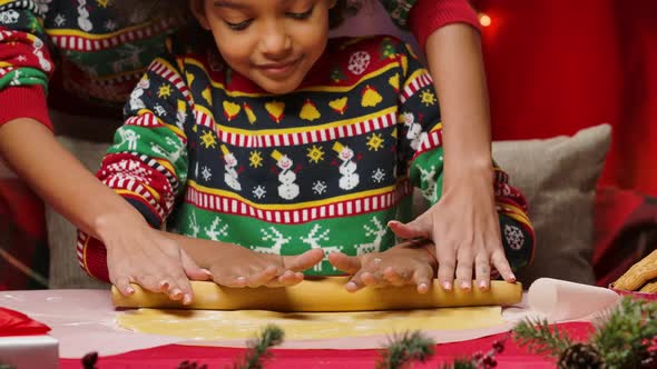 African American Mom and Little Daughter in Bright Holiday Sweaters Roll Out the Dough Together for