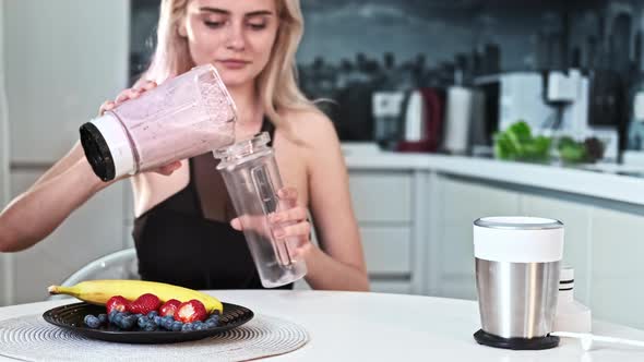 A young blonde woman making a milkshake of fruits and berries