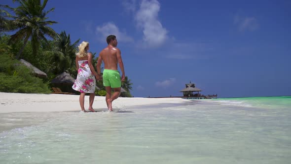 A couple walks on the beach holding hands at a tropical island resort hotel