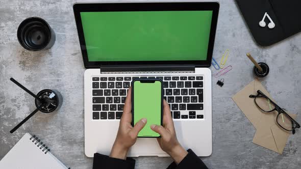 Businesswoman sitting at office work desk, using smartphone with chroma key green screen