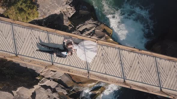 Newlyweds. Bride and Groom Lie on a Bridge Over a Mountain River. Aerial View