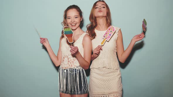 Two young stylish smiling blond women dancing and eating props sweet ice cream