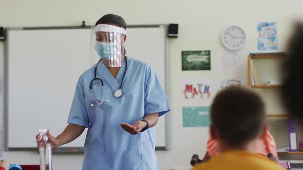 Mixed race female medical worker wearing face mask showing schoolchildren how to disinfect hands