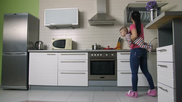 Busy Mother Cooking in Kitchen Holding Baby Son