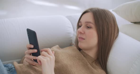 Woman Lying on Couch in Living Room Chatting Writing Message Using Smartphone. Lonely Happy Lady