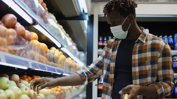 African American Man Standing in Supermarket Putting Apples Into Shopping Basket