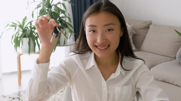 Happy asian apartment owner or renter showing keys and looking at camera