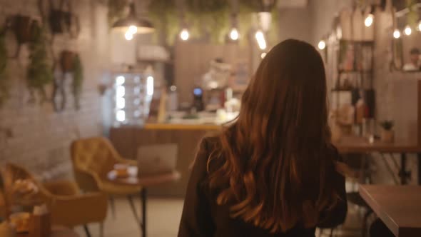 A Beautiful Young Girl Walks Through the Hall of a Cafe Decorated with Living Plants and Sits Down