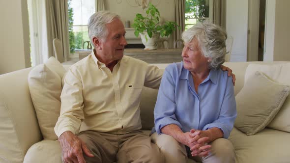 Portrait of smiling caucasian senior couple hugging each other while sitting on the couch at home