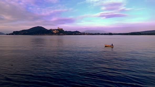 Evocative wide-angle pov of small fishing boat with fisherman rowing in lake waters of Maggiore lake