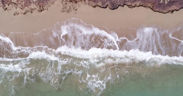 Static top down view of tropical beach, foamy ocean waves washing sand. Waves hitting sand beach