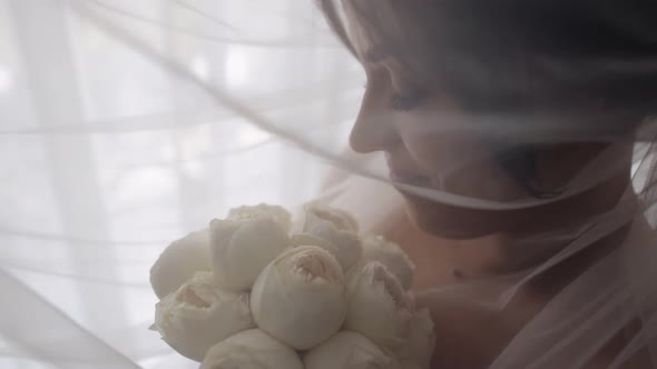 Bride in White Dress Staying Near Window with Flowers Bouquet Wedding Morning Preparations at Home