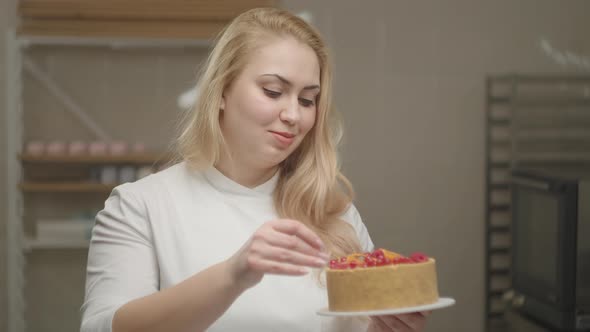 Young Female Confectioner in White Coat Holding Cheesecake Decorated with Apricot and Berries