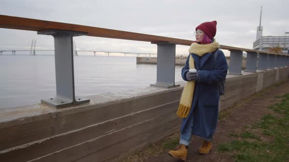 Asian Woman Walking with Coffee Cup along Riverside