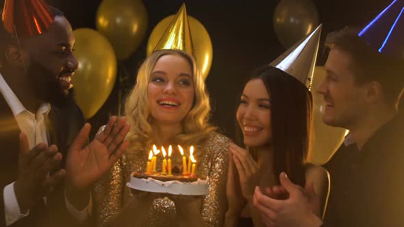 Happy Caucasian Woman in B-Day Hat Blowing Candles on Cake, Friends Applauding