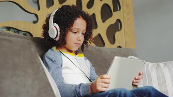 Front view of African american boy with headset playing game on digital tablet in lobby at hospital