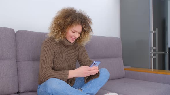 Cheerful white female using modern smartphone with smile on couch at home during lockdown in 4k