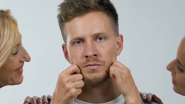 Irritated Man Tolerating Mom and Wife Pinching His Cheeks, Extra Care, Annoyance