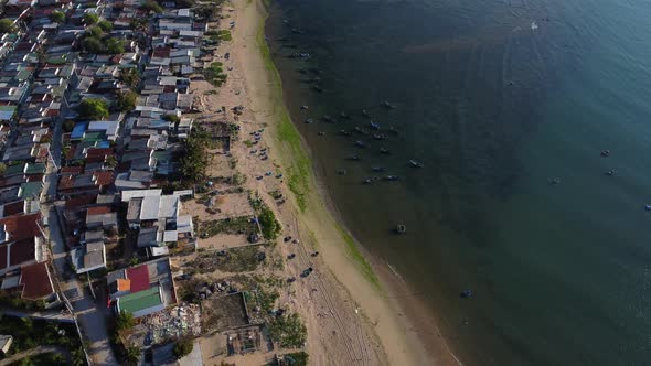 Aerial top down of fisherman town with sandy beach and floating traditional basket boats in ocean -