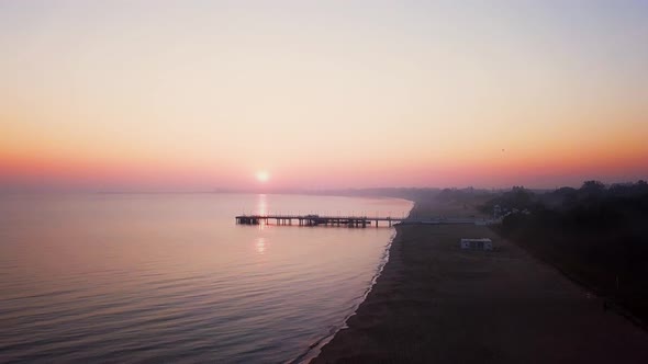 Foggy sunrise over the sea. Hazy morning. Orange sun. Drone footage. Pier shot. Backwards flight ove