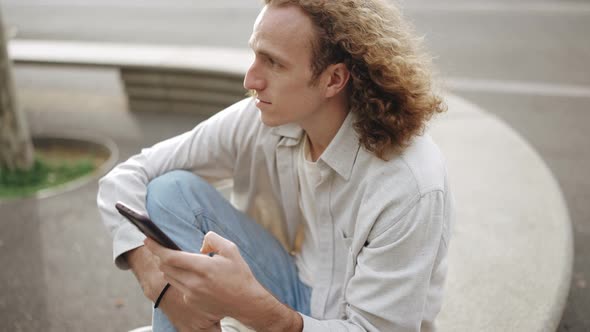 Meditative curly-haired man typing by phone