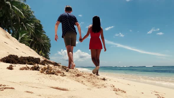 Young Lovers Holding Hands and Talking While Walking on the White Sand Beach.