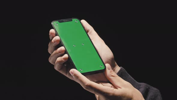 Close-up male hands holding smart phone with green screen. Black background. Mockup screen.