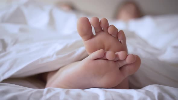Pair of Feet in Bed on White Sheets