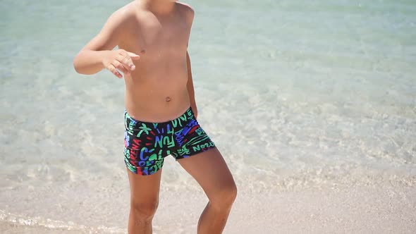 Beautiful Blond Boy in Swimming Shorts Runs Happily Along the Beach. The Concept of a Holiday By the