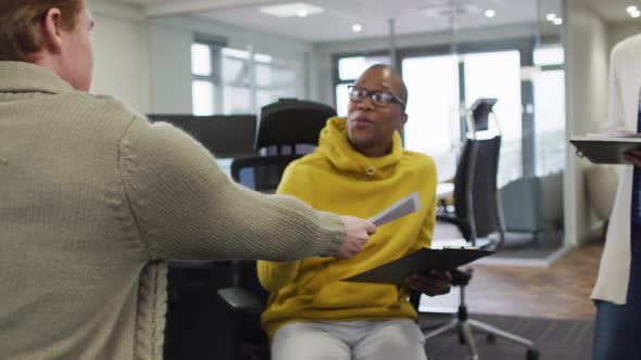 Diverse smiling female business colleagues passing papers and discussing in office