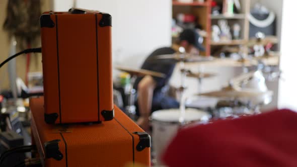 A drummer in a rock and roll garage band playing his instrument with guitar amps and music gear SLOW