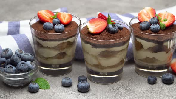 Classic Tiramisu Dessert with Blueberries and Strawberries in a Glass on Concrete Background